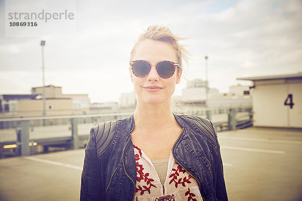 Porträt einer mittel-erwachsenen Frau mit Sonnenbrille auf einem Parkplatz auf dem Dach