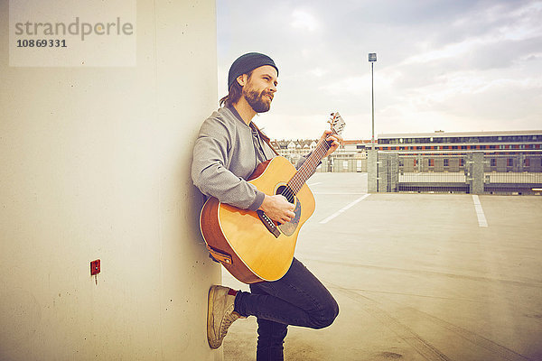 Mittelgroßer Mann spielt Akustikgitarre auf dem Parkplatz auf dem Dach