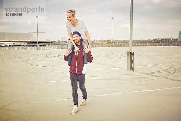 Mittelgroßer Erwachsener  der seine Freundin auf dem Parkplatz auf dem Dach über die Schulter nimmt