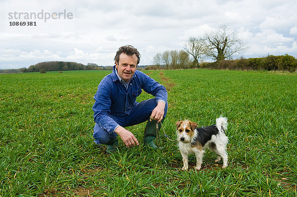 Porträt eines auf dem Feld kauernden Bauern mit Hund