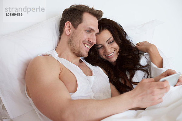 Junges Paar sitzt im Bett und stöbert auf einem digitalen Tablet