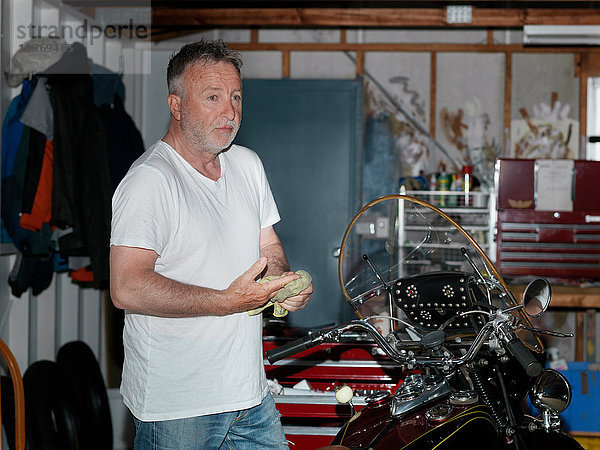 Älterer Mann wischt sich bei Motorradreinigung in Garage die Hände