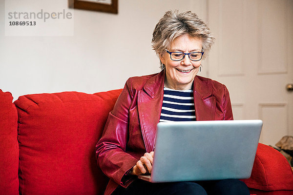 Ältere Frau auf Wohnzimmer-Sofa beim Tippen am Laptop