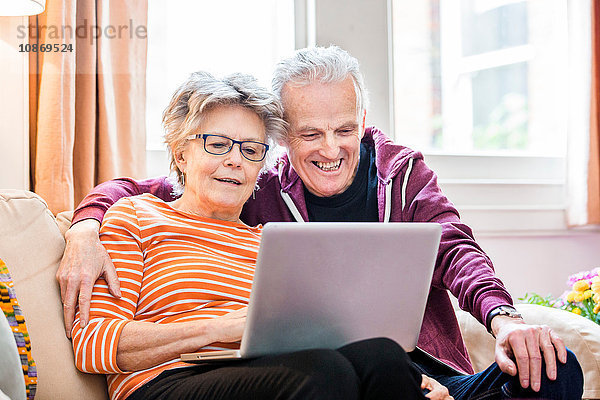Älteres Ehepaar auf Wohnzimmer-Sofa mit Blick auf Laptop