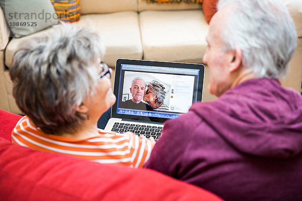 Über-Schulter-Ansicht eines älteren Paares auf einem Wohnzimmersofa beim Betrachten von Fotos auf einem Laptop