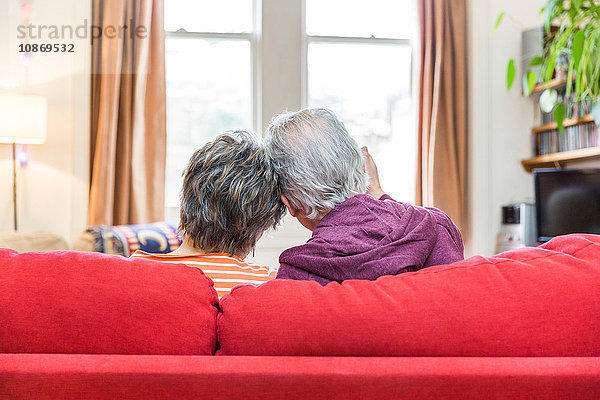 Rückansicht eines romantischen Seniorenpaares auf einem Wohnzimmersofa mit verbundenen Köpfen