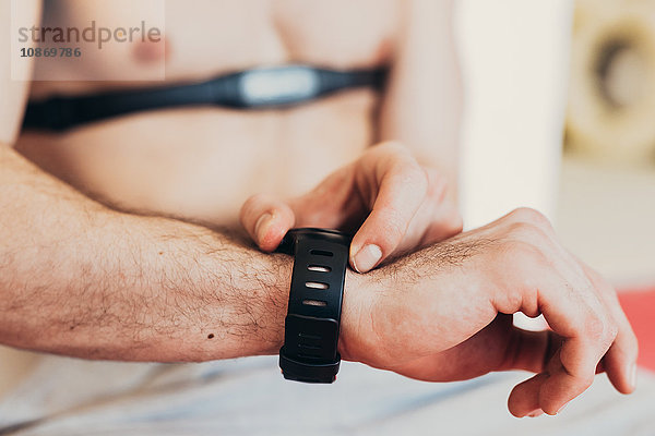 Mann trägt Herzfrequenzmessgerät an Brustkorb und überprüft Armbanduhr