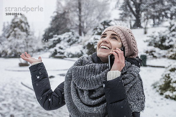 Frau in schneebedeckter Landschaft telefoniert mit Smartphone