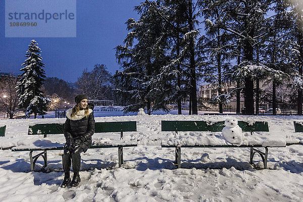 Frau sitzt abends auf Parkbank im überdachten Park