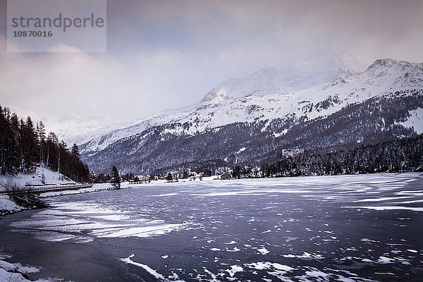 Gefrorener See und Dorf unter einem schneebedeckten Berg  Engadin  Schweiz