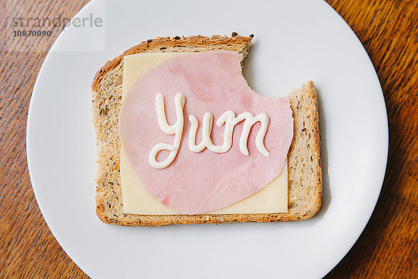 Draufsicht auf das Wort Yum auf Schinken und Käse auf Brot in Mayonnaise