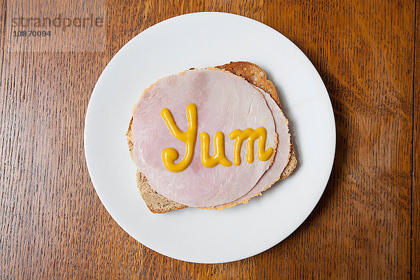 Draufsicht auf das Wort yum geschrieben auf Schinken auf Toast in Senf