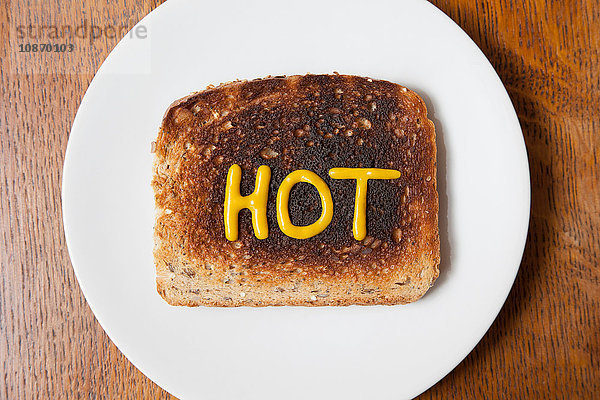 Draufsicht auf das in Senf geschriebene Wort heiß auf verbranntem Toast