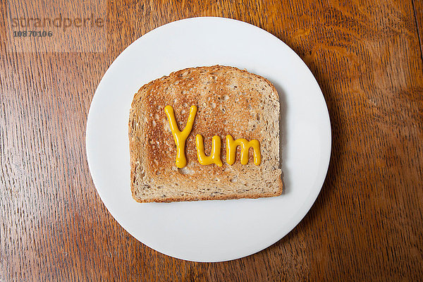 Draufsicht auf das Wort yum geschrieben auf Schinken auf Toast in Senf