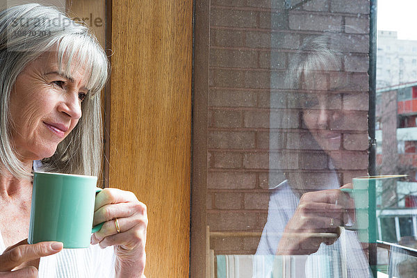 Frau mit Becher  durchs Fenster schauend