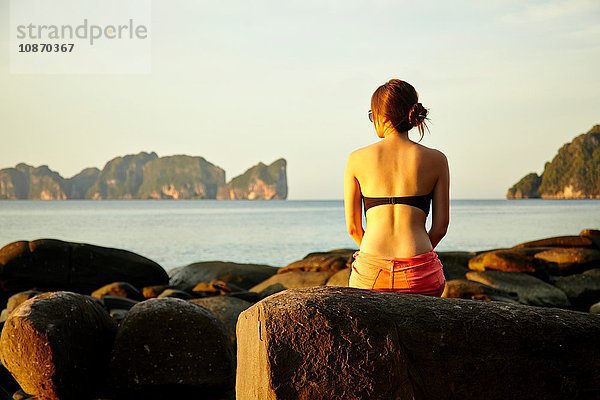 Junge Frau sitzt auf einem Küstenfelsen  Phi Phi-Inseln  Thailand