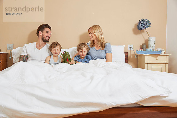 Mutter und Vater im Bett mit Söhnen und Spielzeugdrachen
