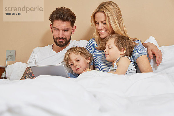 Mutter und Vater im Bett mit Söhnen  die auf ein digitales Tablet schauen