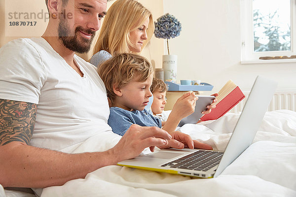 Mutter und Vater im Bett mit Söhnen  die Technik nutzen  Buch lesen