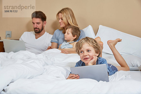 Mutter und Vater im Bett mit Söhnen mit Technologie