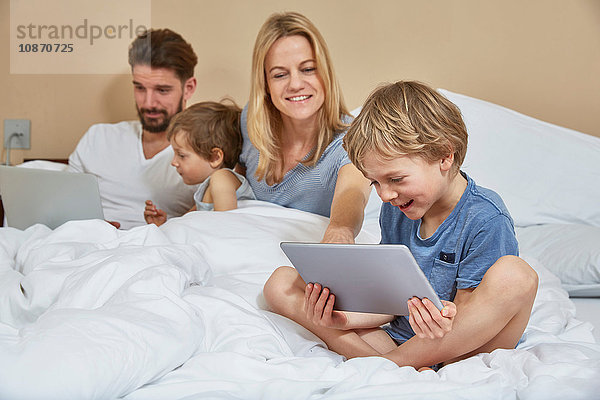 Mutter und Vater im Bett mit Söhnen mit Technologie