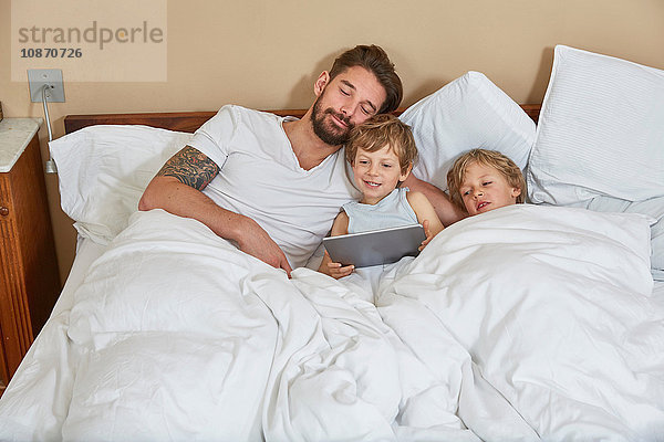 Vater und Söhne im Bett mit digitalem Tablett