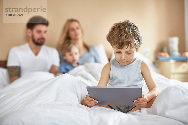 Junge am Bett der Eltern mit digitalem Tablett