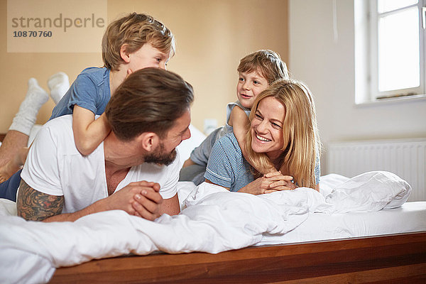Jungen im Bett  die auf den Eltern liegen und von Angesicht zu Angesicht lächeln