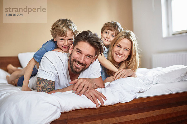 Jungen im Bett liegend auf Eltern  die lächelnd in die Kamera schauen