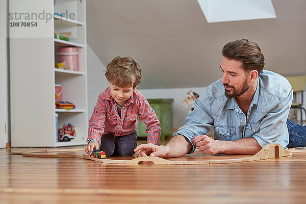 Vater und Sohn spielen mit einer Spielzeugeisenbahn aus Holz