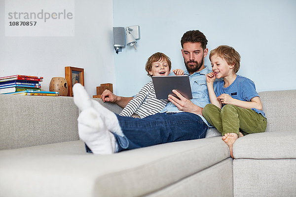 Vater und Söhne auf Sofa mit digitalem Tablett