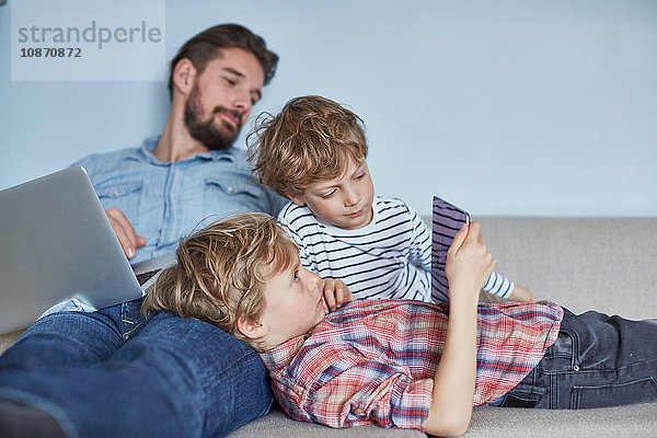 Jungen  die mit ihrem Vater auf dem Sofa liegen und Technik nutzen