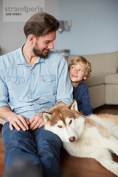 Vater und Sohn sitzen mit lächelndem Hund von Angesicht zu Angesicht