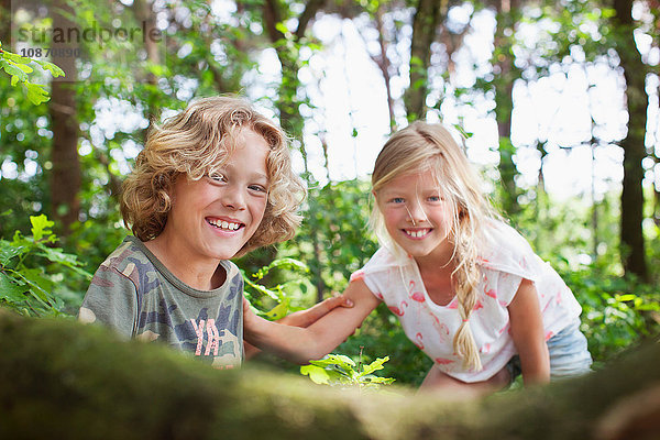 Junge und Mädchen im Wald schauen lächelnd in die Kamera