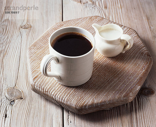 Tasse schwarzer Kaffee und Milchkännchen auf Schneidebrett
