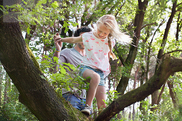 Vater hilft Tochter beim Klettern auf Baum