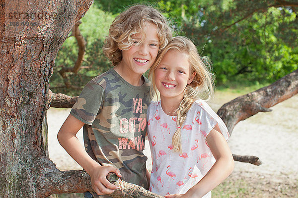 Junge und Mädchen neben dem Baum schauen lächelnd in die Kamera