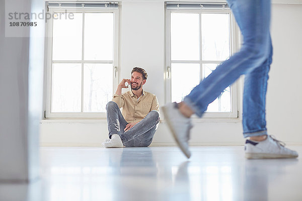 Mann sitzt auf dem Boden und unterhält sich mit einem Smartphone in der neuen Wohnung