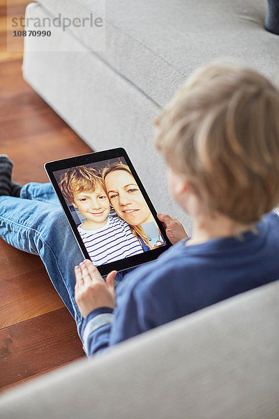 Junge sitzt auf dem Boden und unterhält sich mit Mutter und Bruder über ein digitales Tablet-Videogespräch