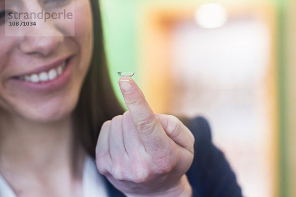 Frau hält Kontaktlinse am Finger und lächelt
