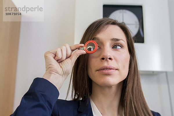 Frau im Büro eines Optikers schaut durch ein optisches Werkzeug