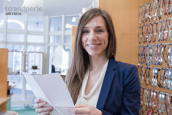 Verkaufsassistentin bei Optikern hält Papierkram in der Hand und schaut lächelnd in die Kamera