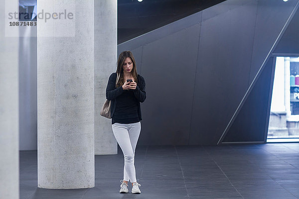 Vorderansicht einer Frau in voller Länge  die stehend auf einem Smartphone simst
