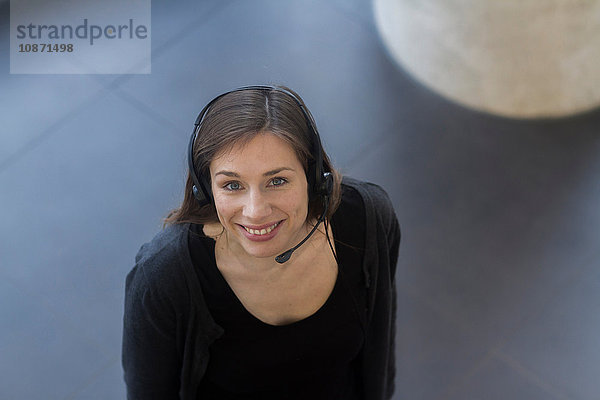 Hochwinkelansicht einer Frau mit Telefon-Headset  die lächelnd in die Kamera schaut