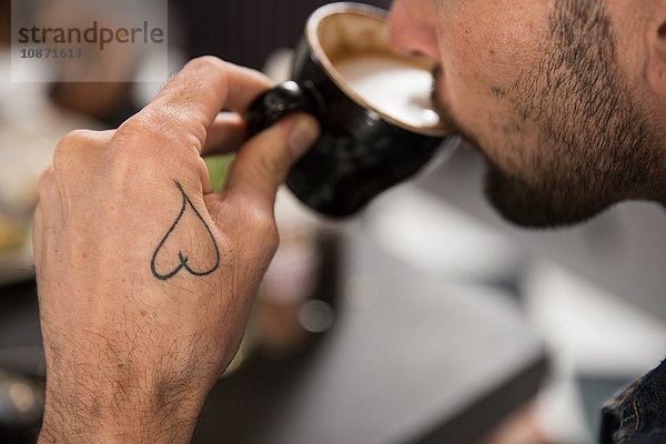 Ausschnitt eines tätowierten Mannes beim Kaffeetrinken
