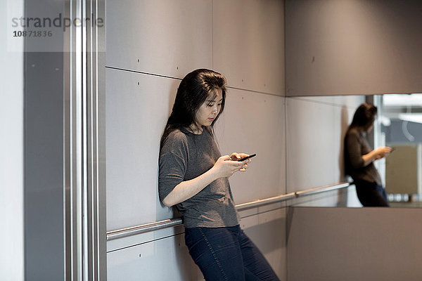 An die Wand gelehnte Frau  die ein Smartphone benutzt