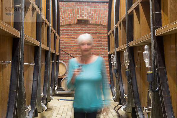 Ältere Frau geht durch den Weinkeller  hält ein Glas Wein  verschwommene Bewegung