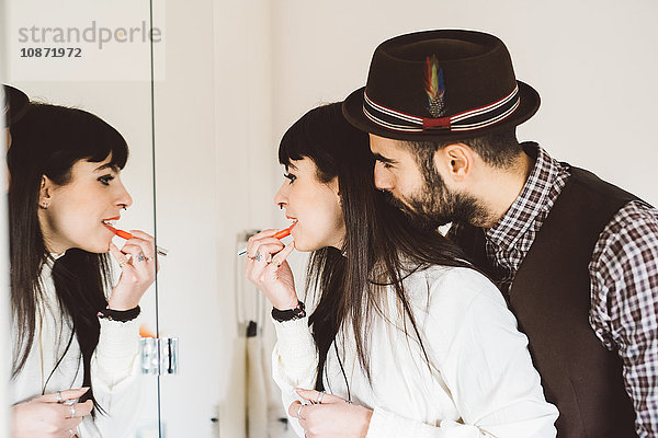 Junger Mann mit Frau  die vor dem Spiegel Lippenstift aufträgt