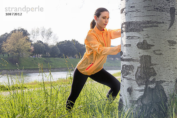 Junge Frau  die im Freien trainiert und sich gegen einen Baum streckt