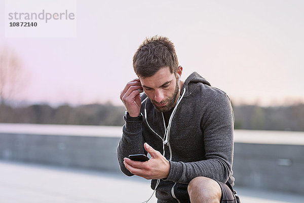 Mittelgroßer erwachsener Mann  im Freien  Smartphone anschauend  Kopfhörer tragend